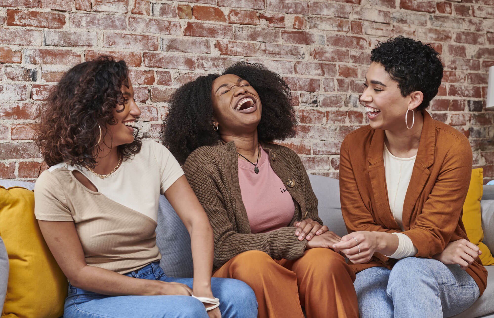 Image of three women laughing while sitting on a sofa.