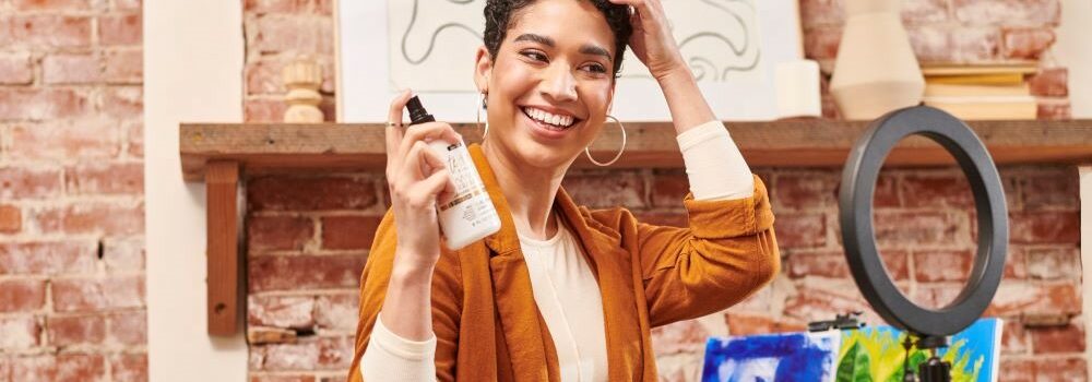 Woman in front of ring light and camera demonstrating how she uses Texture Theory Curl Refresher Spray