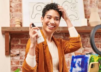 Woman in front of ring light and camera demonstrating how she uses Texture Theory Curl Refresher Spray